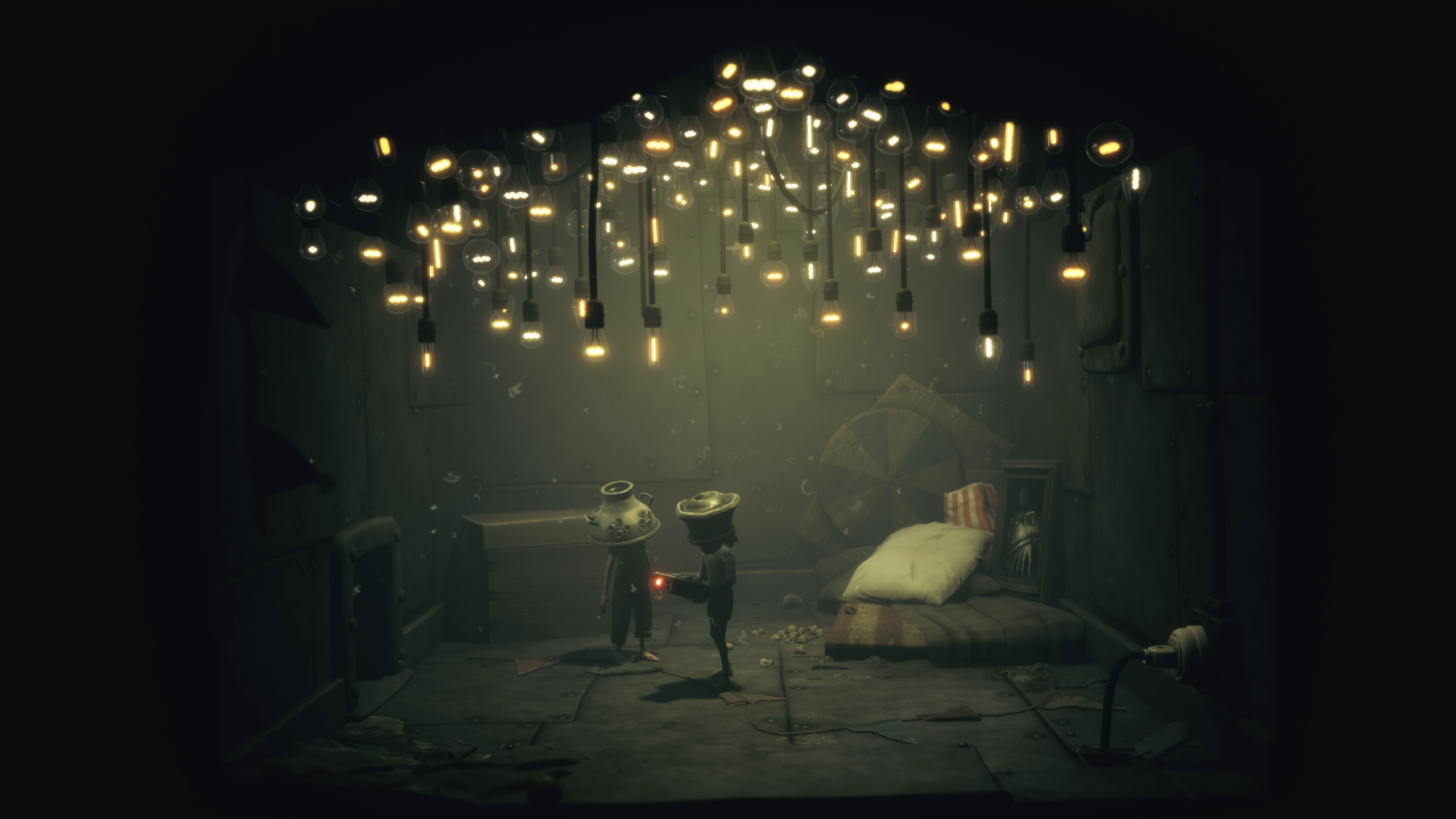 Little Nightmares III : un premier contenu additionnel 2 Capture d'écran du contenu additionnel de Little Nightmares III : The Backstage, montrant les deux enfants dans une pièce au plafond recouvert de petites lumières douces. Il semble s'agir d'une chambre de fortune avec quelques objets collectionnés et un matelas au sol.