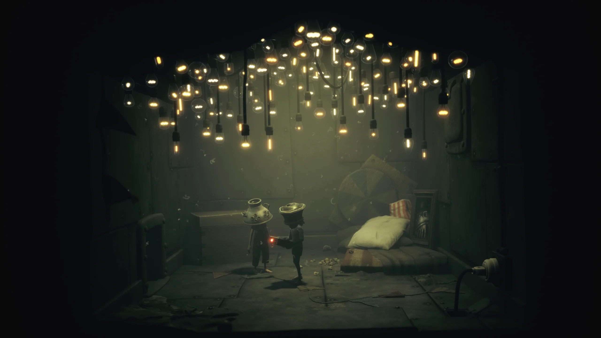 Little Nightmares III : un premier contenu additionnel 2 Capture d'écran du contenu additionnel de Little Nightmares III : The Backstage, montrant les deux enfants dans une pièce au plafond recouvert de petites lumières douces. Il semble s'agir d'une chambre de fortune avec quelques objets collectionnés et un matelas au sol.