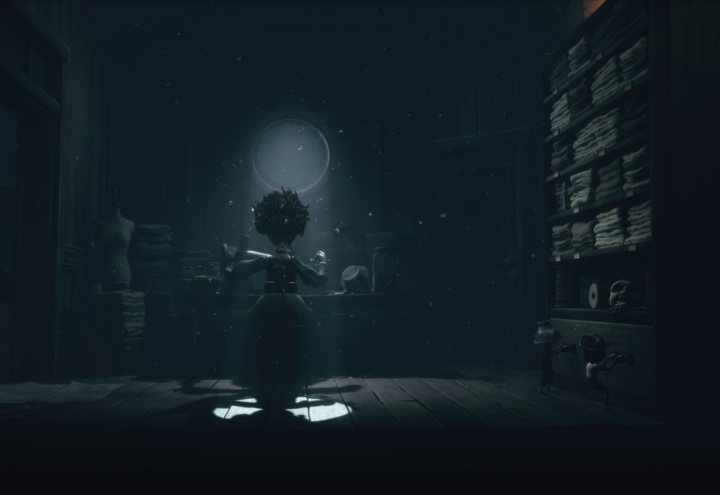 Capture d'écran du contenu additionnel de Little Nightmares III : The Backstage. Une couturière est à l'oeuvre, de dos, dans une pièce très sombre où seul une légère lumière provient d'une petite fenêtre, mettant en valeur la femme en plein travail.